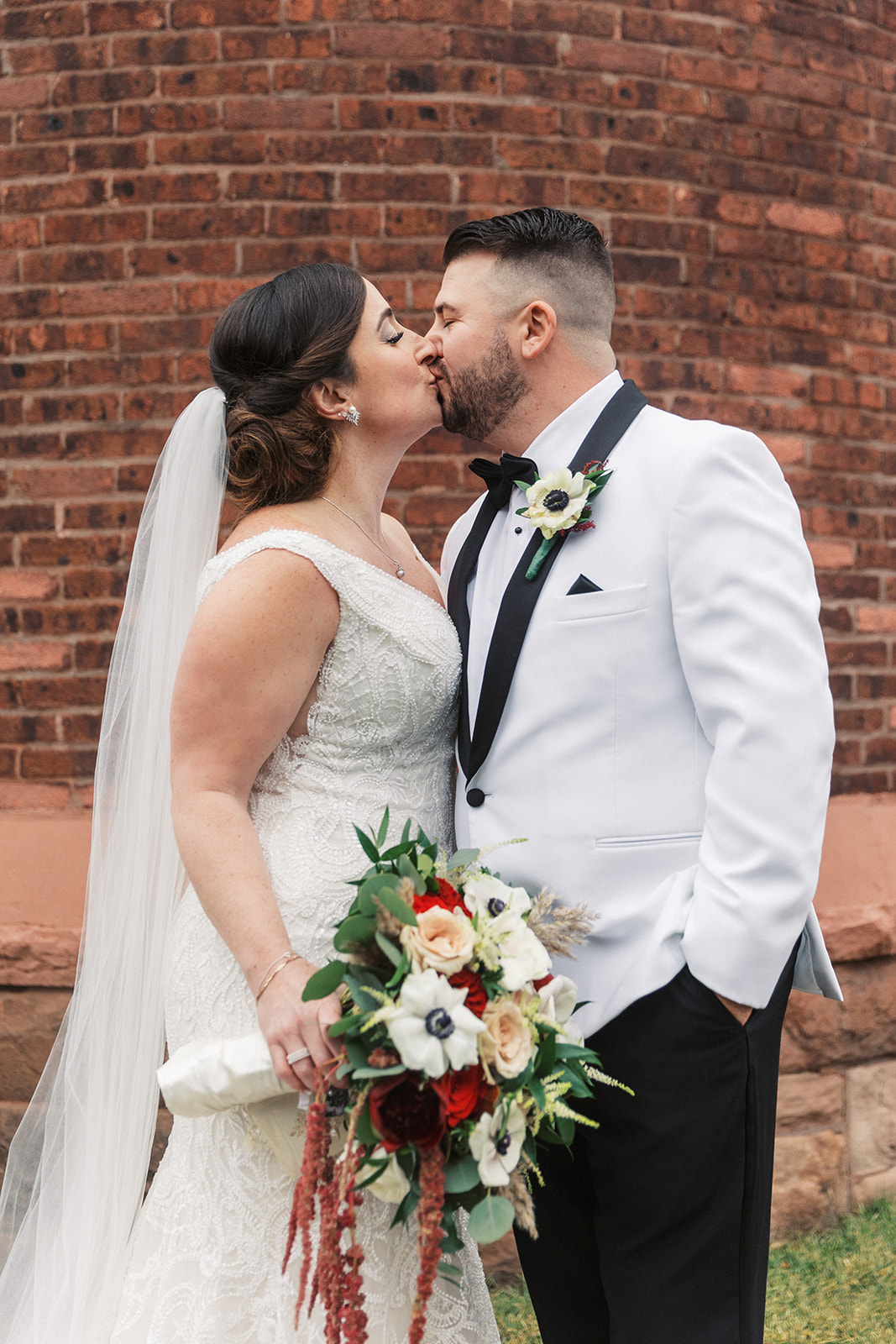 Newlyweds kiss in front of a brick wall at an Above Weddings