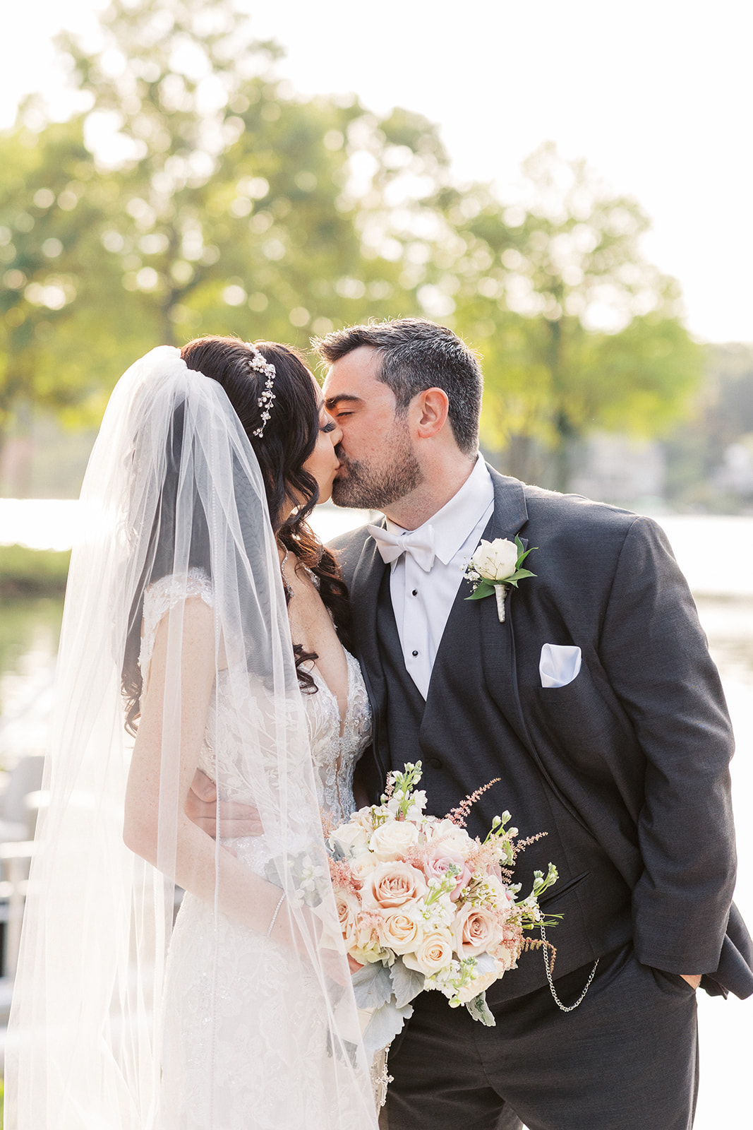 Newlyweds kiss while standing in a waterfront garden