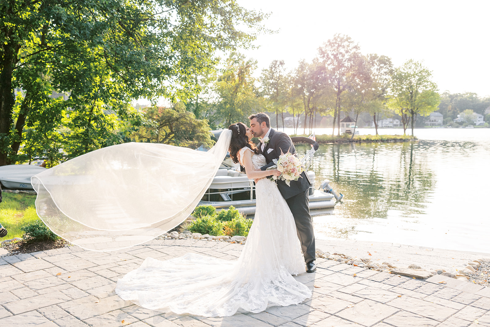 Newlyweds kiss in a waterfront garden as the veil blows in the wind at their Seasons Catering Wedding