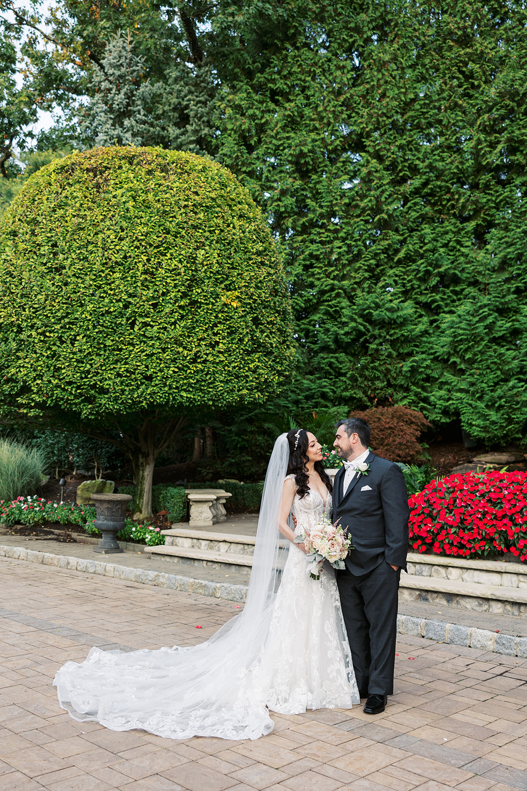Newlyweds stand together in a black suit and lace dress in a garden patio at their Seasons Catering Wedding