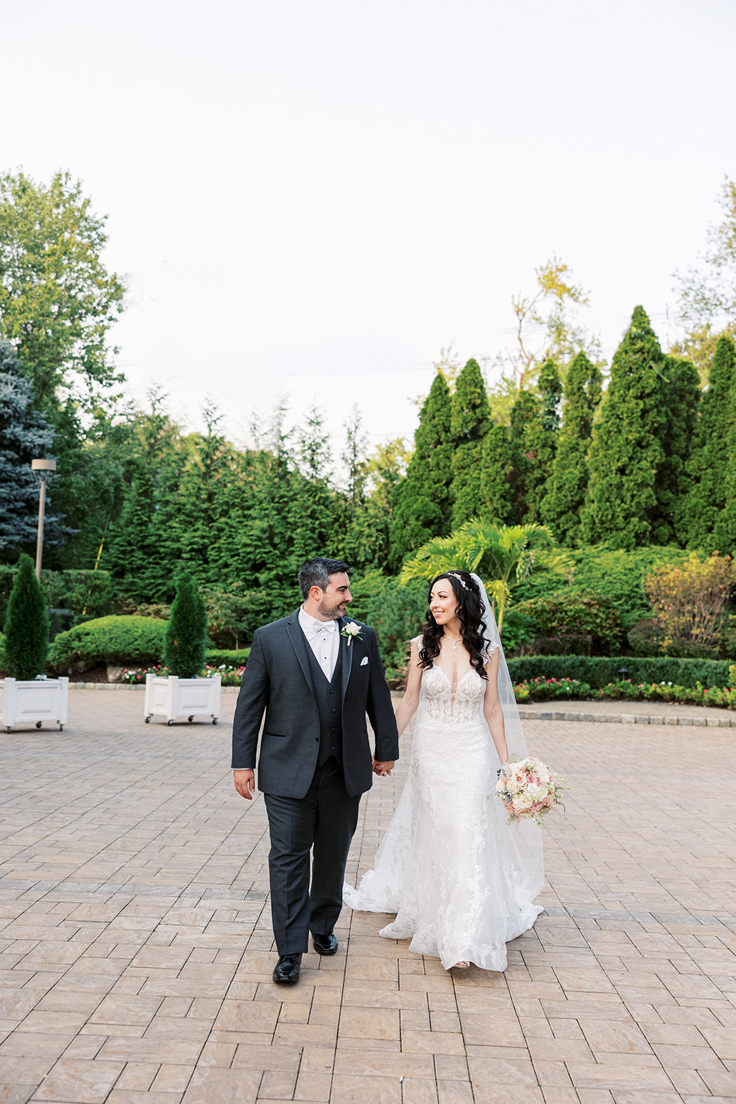 Newlyweds walk through a garden patio holding hands and smiling at each other at their Seasons Catering Wedding