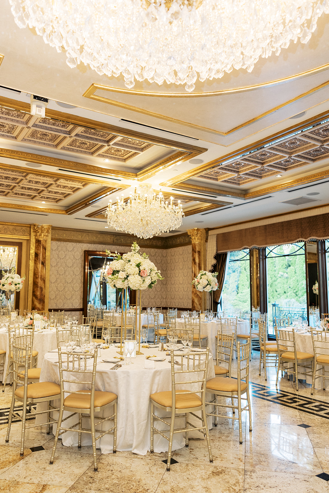 A wedding reception set up with gold chairs and white linens under large chandeliers