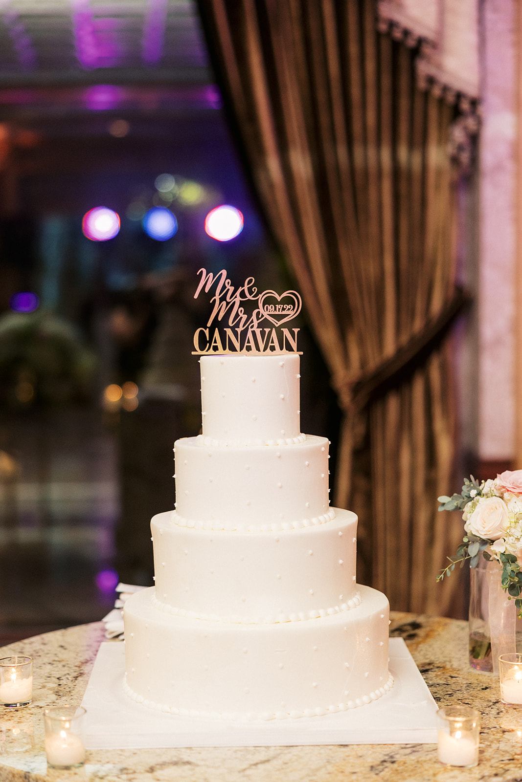 A four tier cake sits on a granite table with custom topper