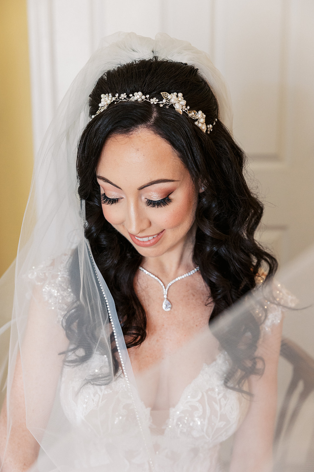A bride sits in a wooden chair getting ready in her embroidered lace dress