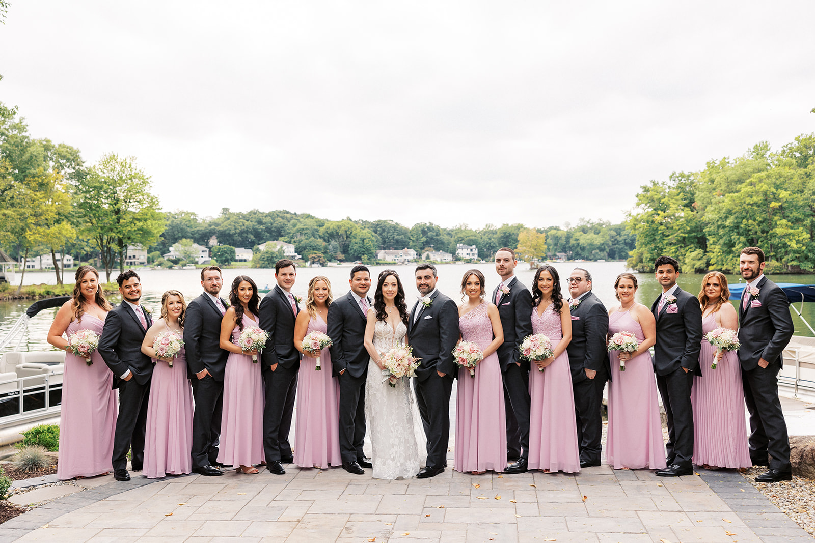 Newlyweds stand in between their large wedding part on a waterfront patio
