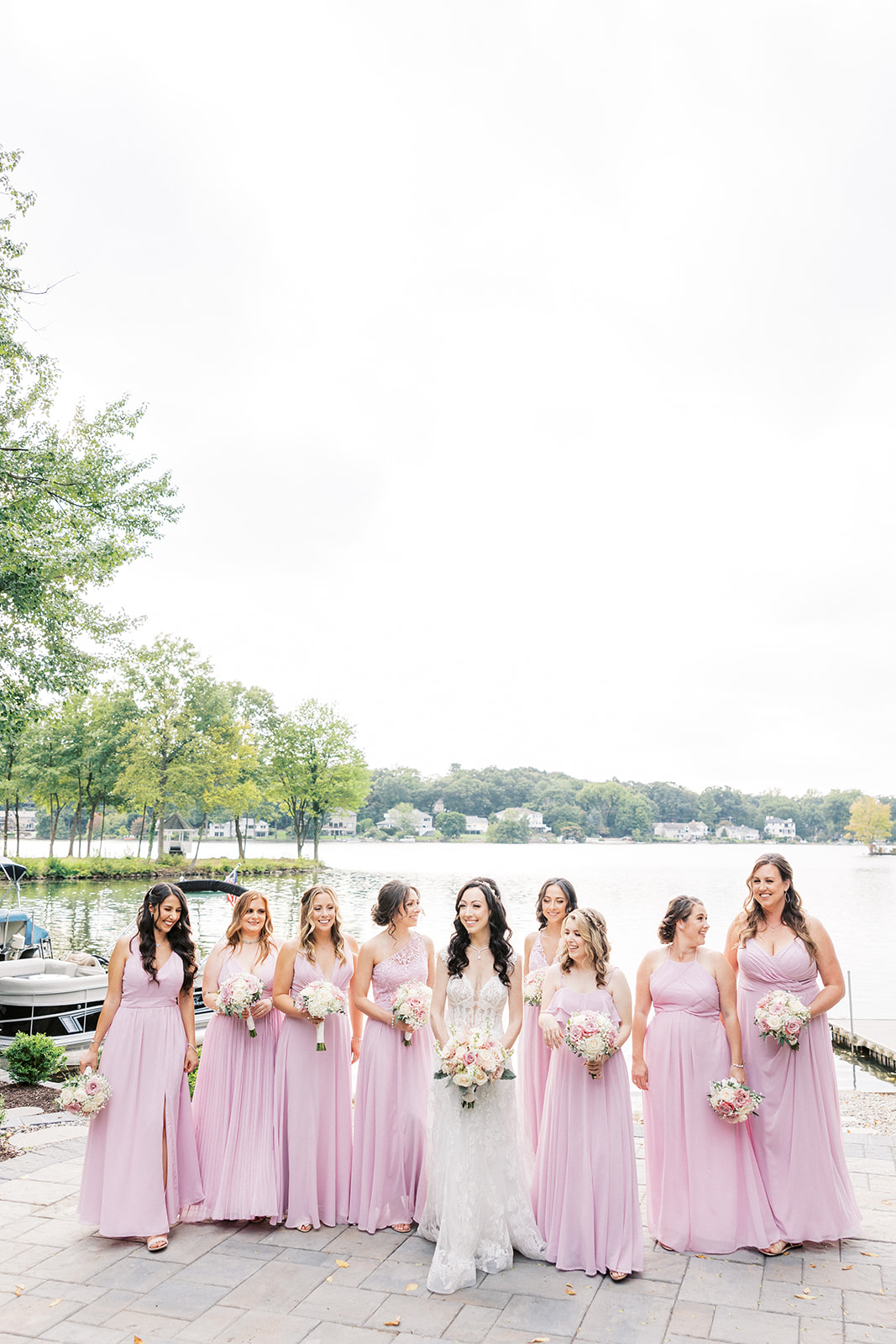 A bride stands with her 8 bridesmaids in pink dresses on a waterfront patio Seasons Catering Wedding