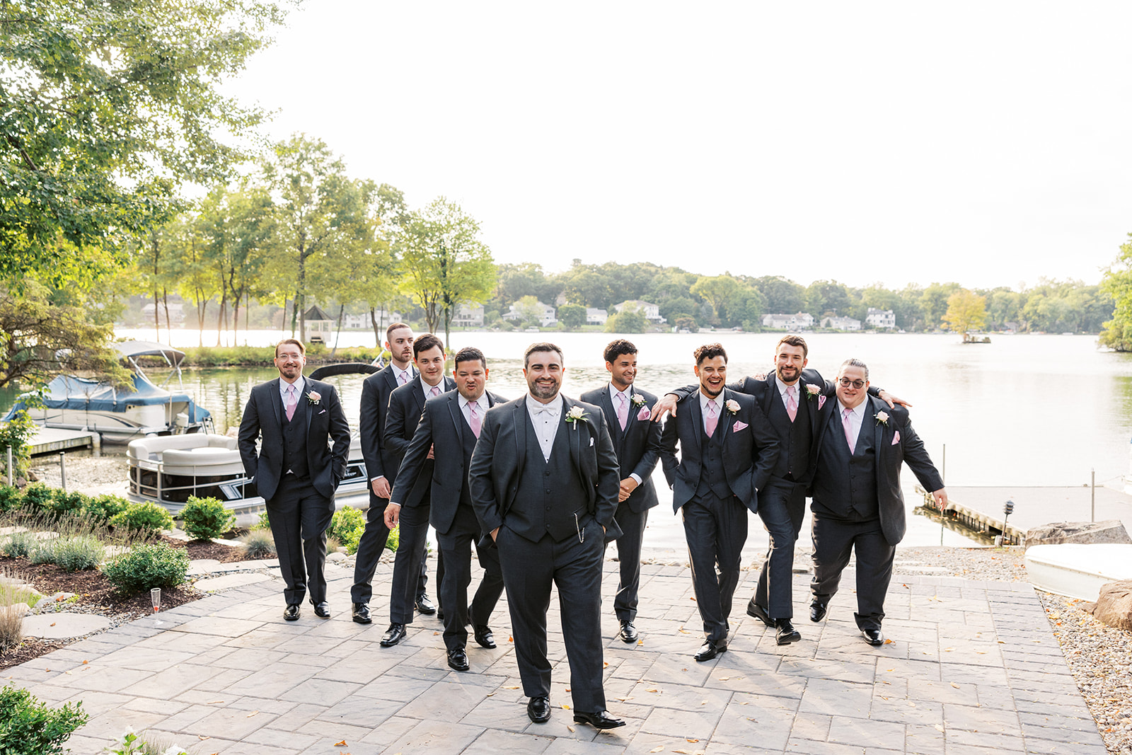 A groom walks through a patio laughing with his 9 groomsemen at his Seasons Catering Wedding