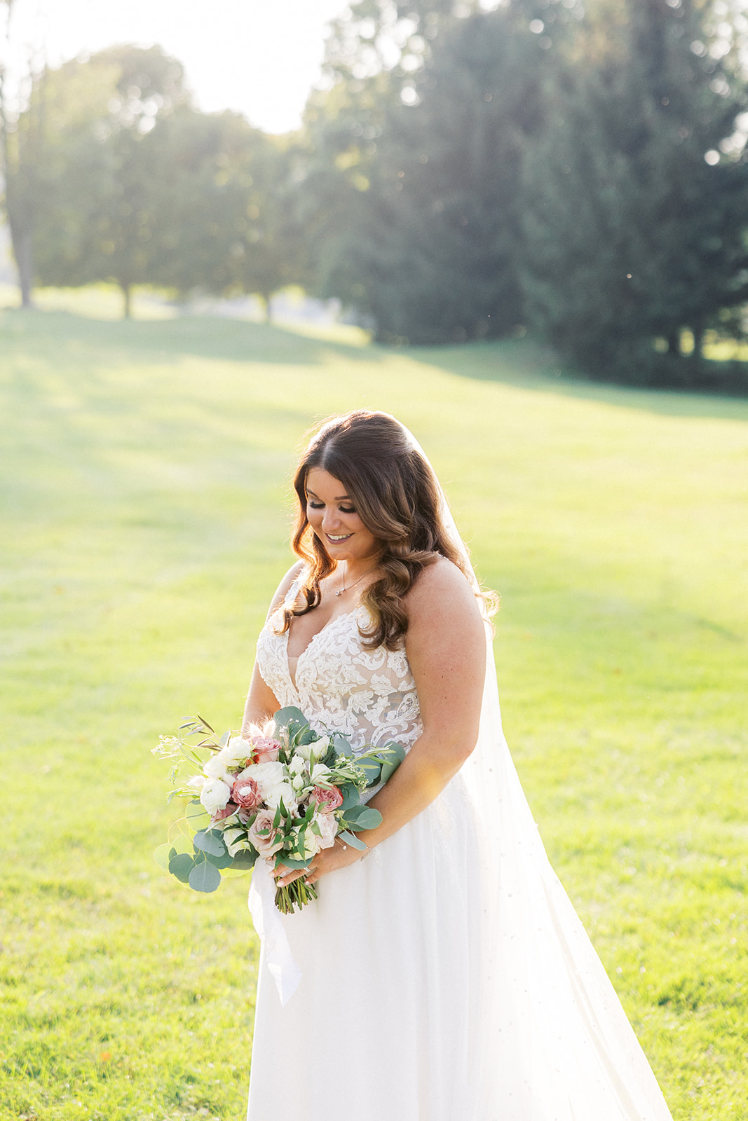 A bride smiles down at her flowers while standing on a golf course at her Skyview Golf Club Wedding