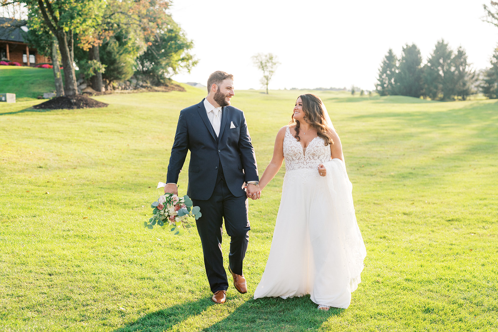 Newlyweds walk down a fairway holding hands at sunset during their Skyview Golf Club Wedding