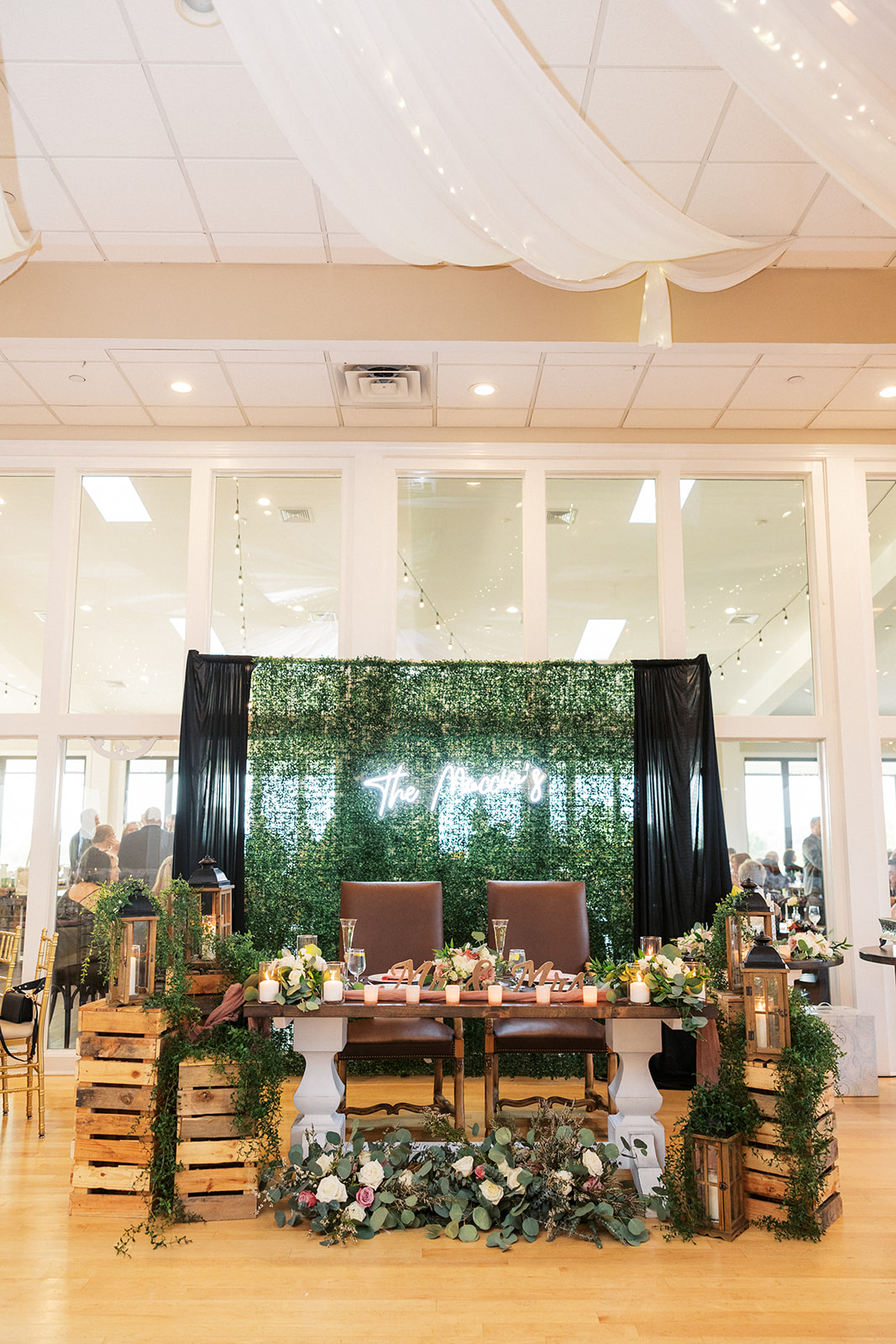 Details of a wedding head table covered in greenery in front of a greenery wall