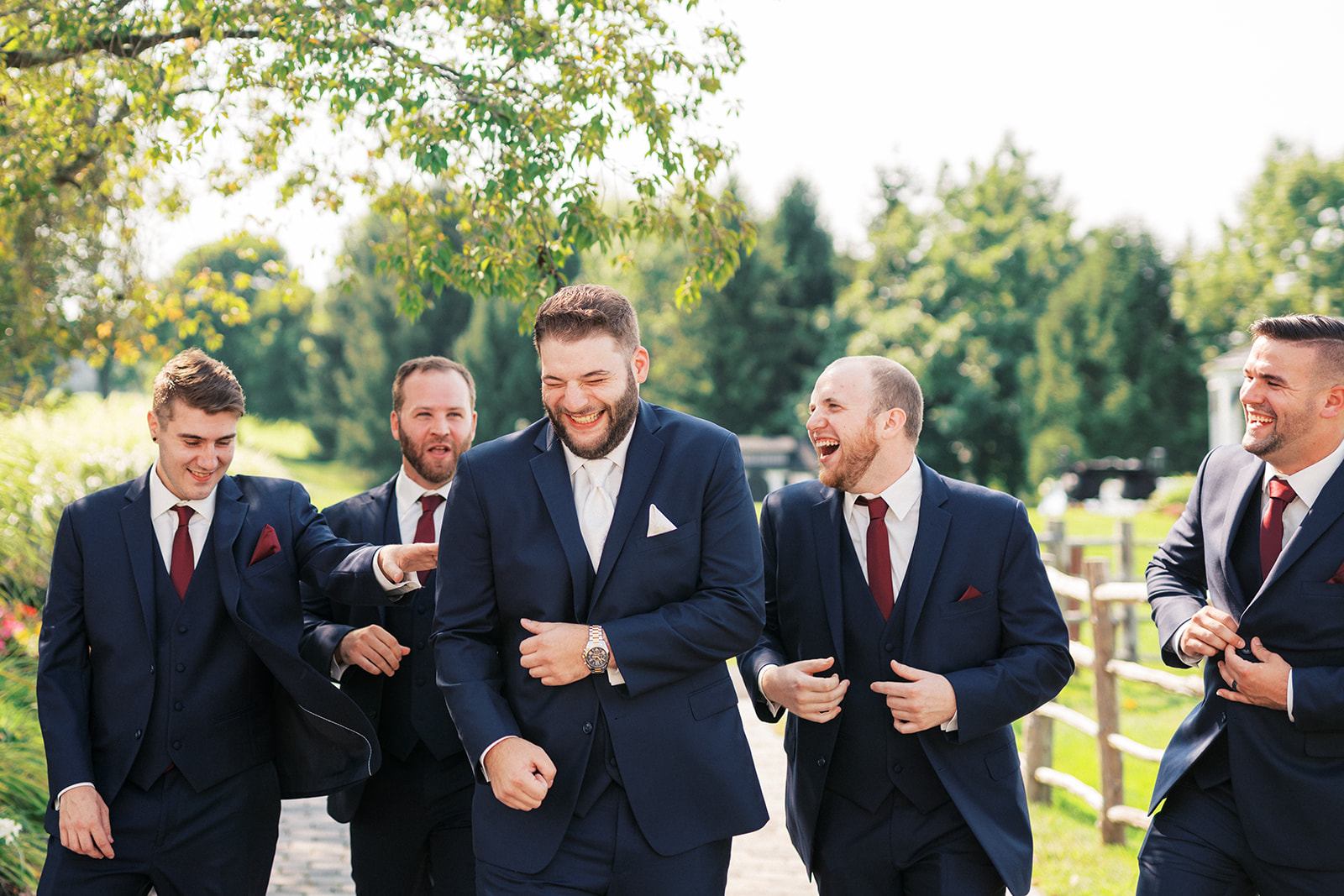 A groom laughs while walking down a garden path with his groomsmen at his Skyview Golf Club Wedding