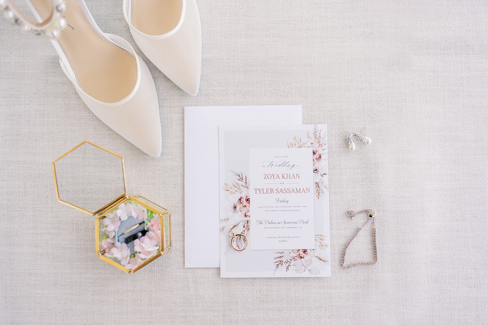 Details of a bride's earrings, shoes and jewelry on a white mat
