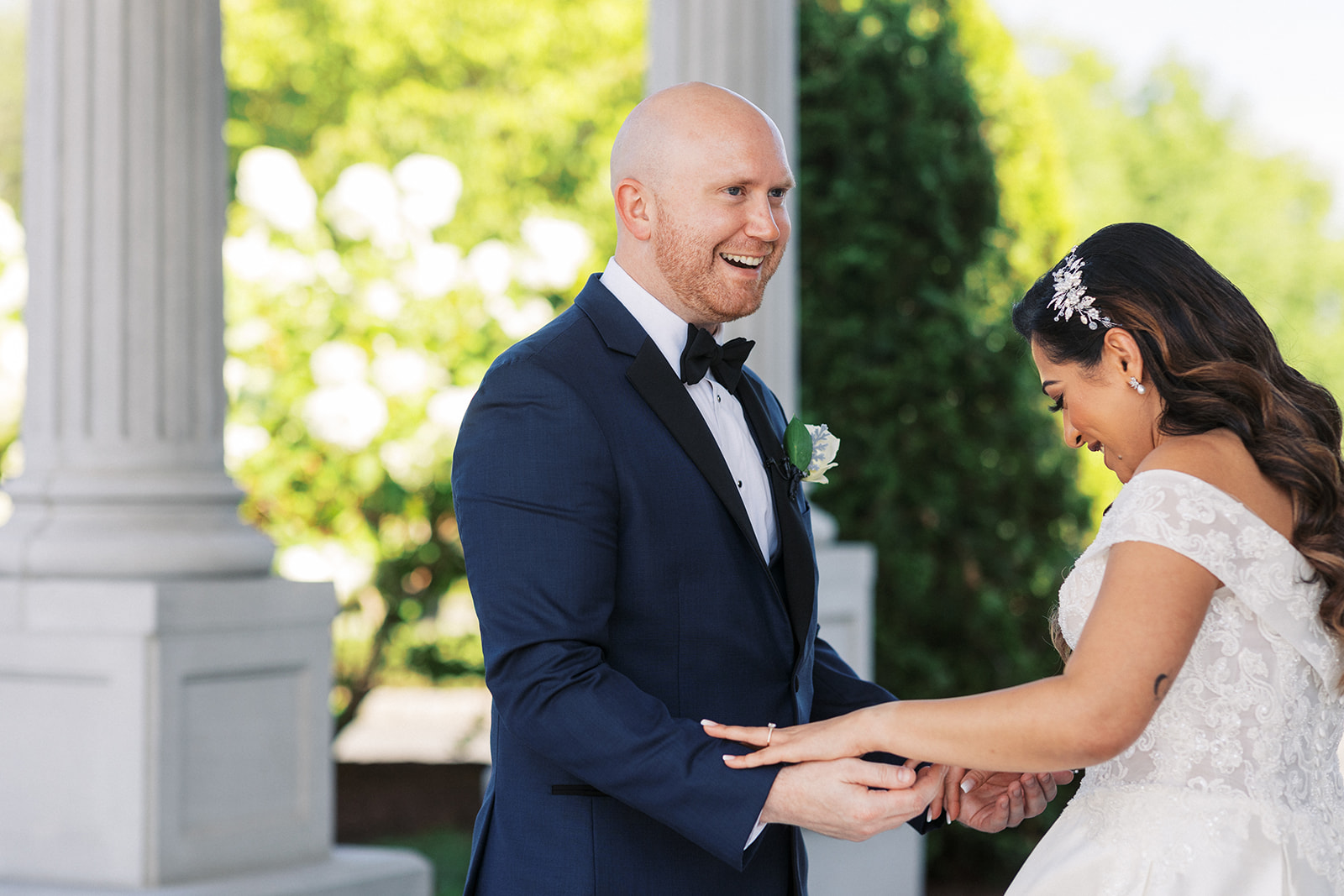 A bride and groom smile big during their first look in a garden