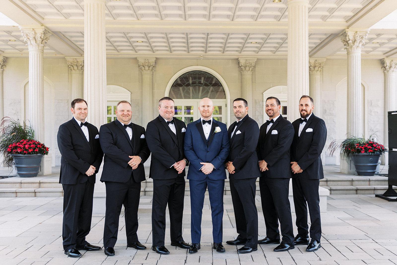 A groom stands with hands crossed in an ornate carport with his 6 groomsmen