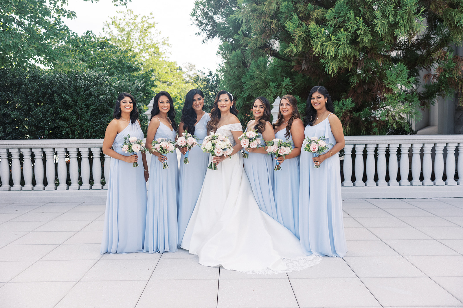 A bride stands with her 6 bridesmaids on a garden terrace holding their bouquets at a The Palace At Somerset Wedding