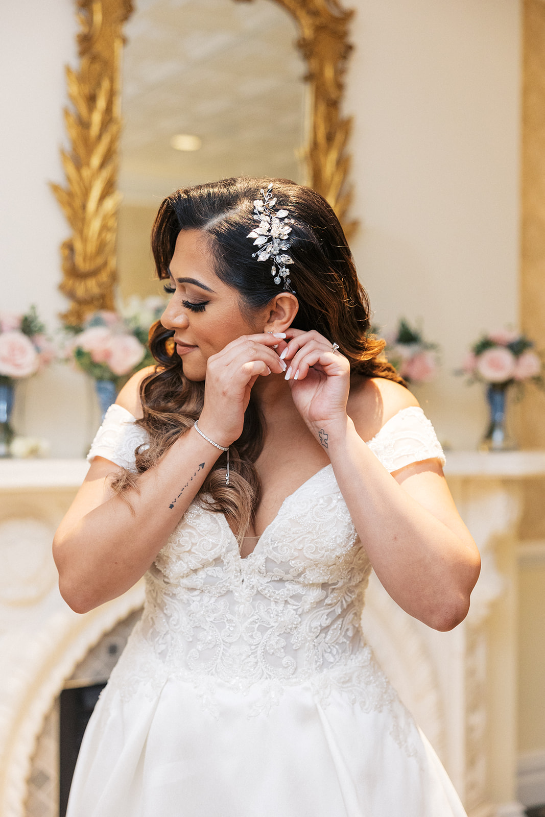 A bride stands in an ornate dressing room putting on her earrings at her The Palace At Somerset Wedding