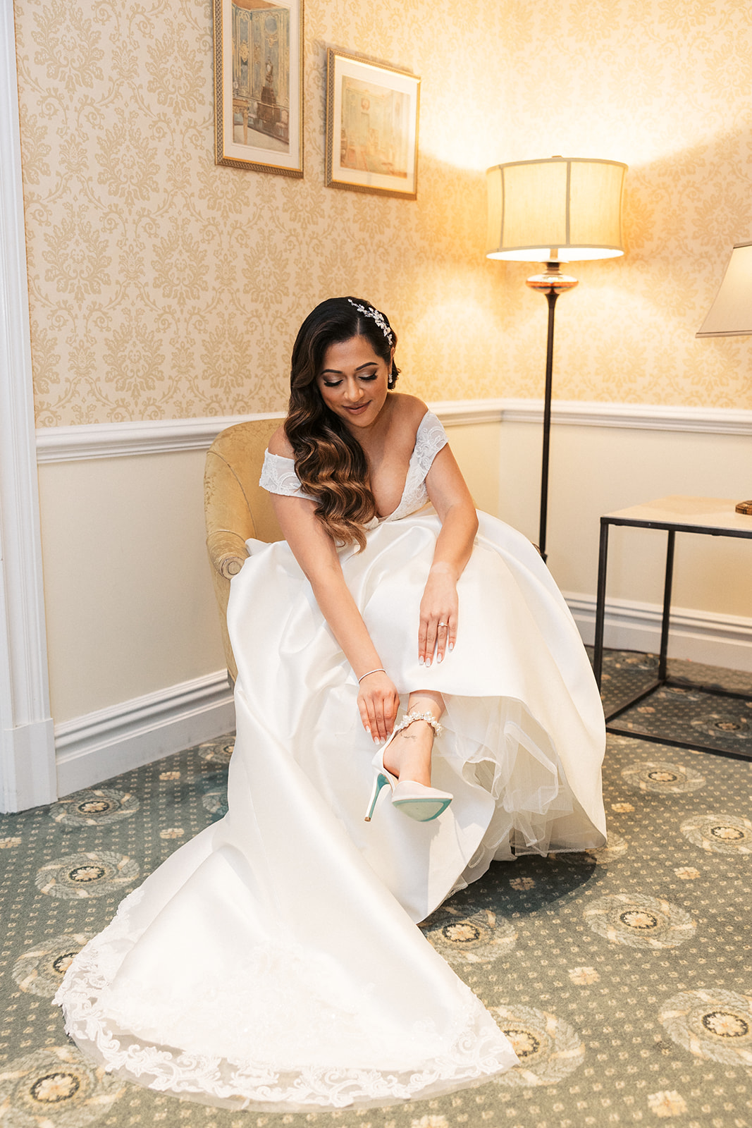 A bride puts on her shoes in her dress while getting ready for her The Palace At Somerset Wedding