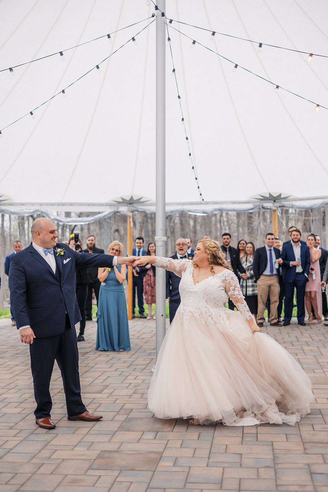 Newlyweds dance while holding hands under a large white tent on a brick patio at their reception