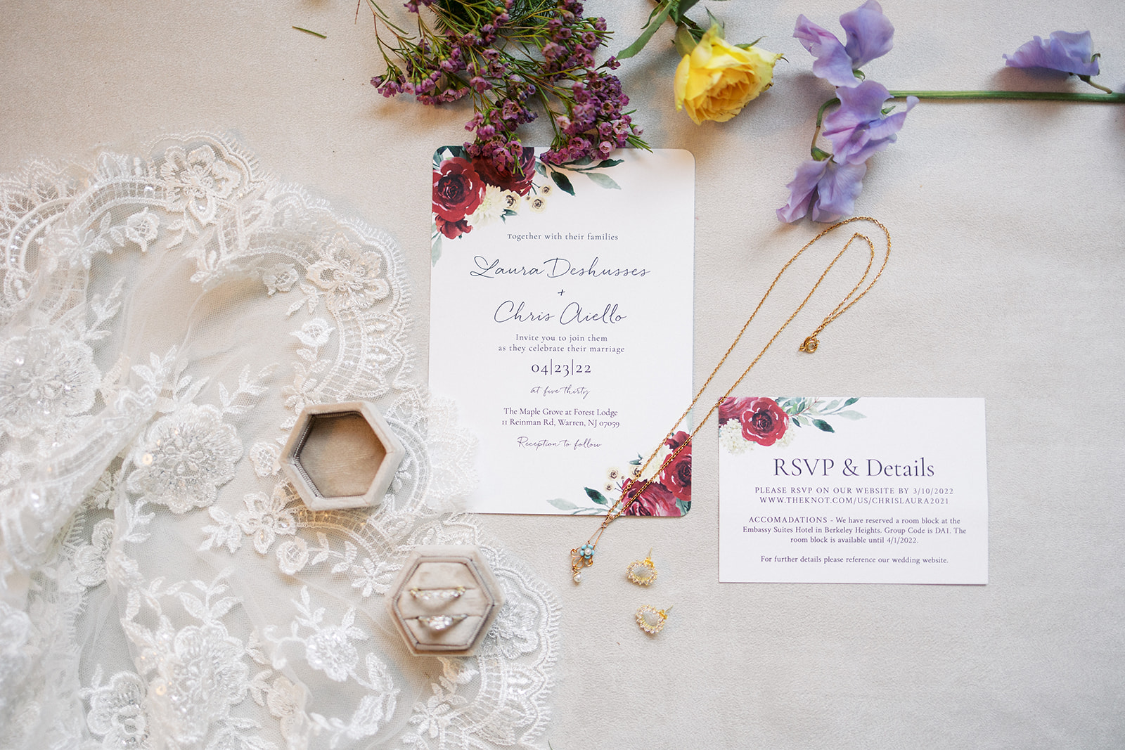 Details of lace jewelry and flowers sit on a table with wedding invitations