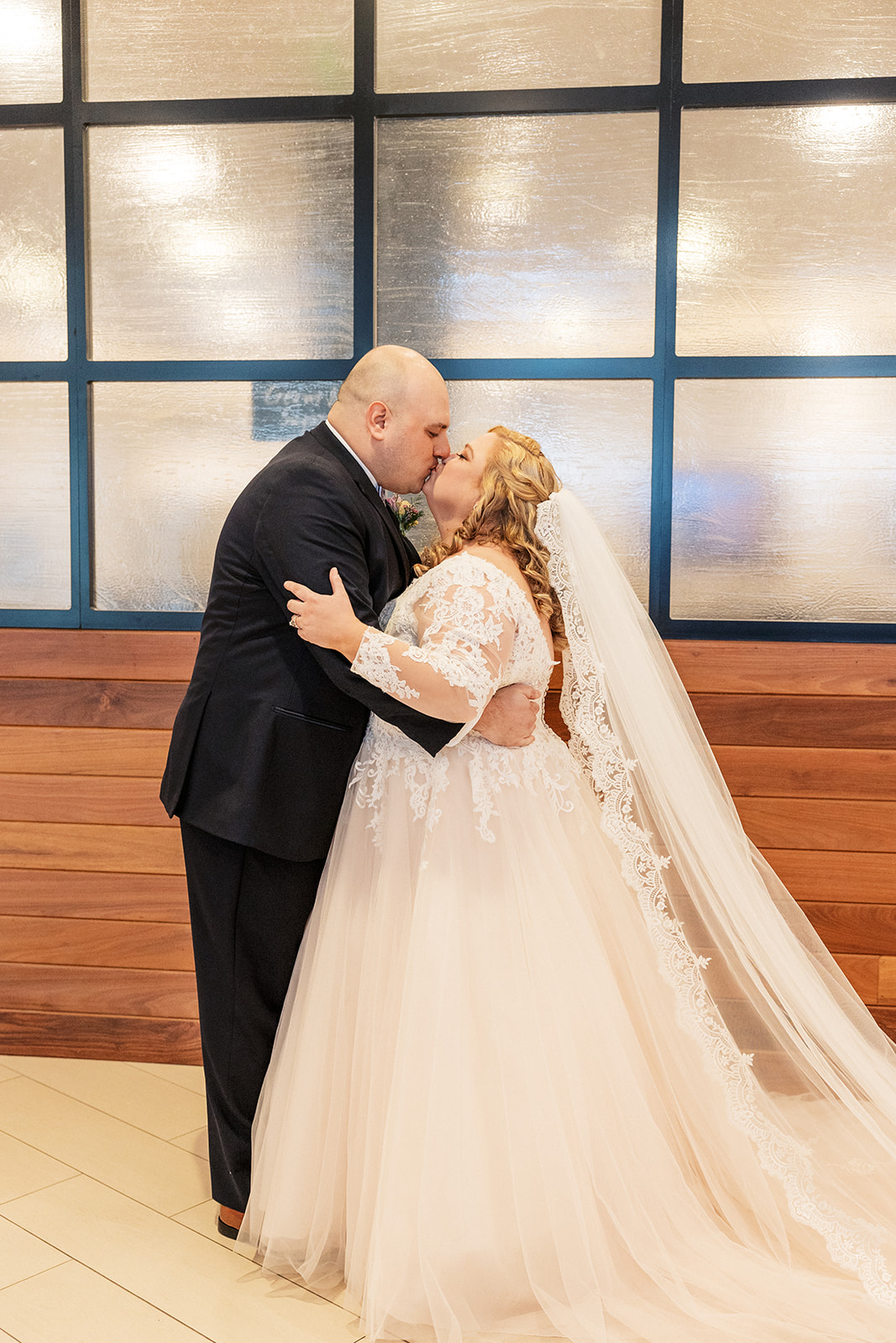 Newlyweds kiss against a wooden wall with windows