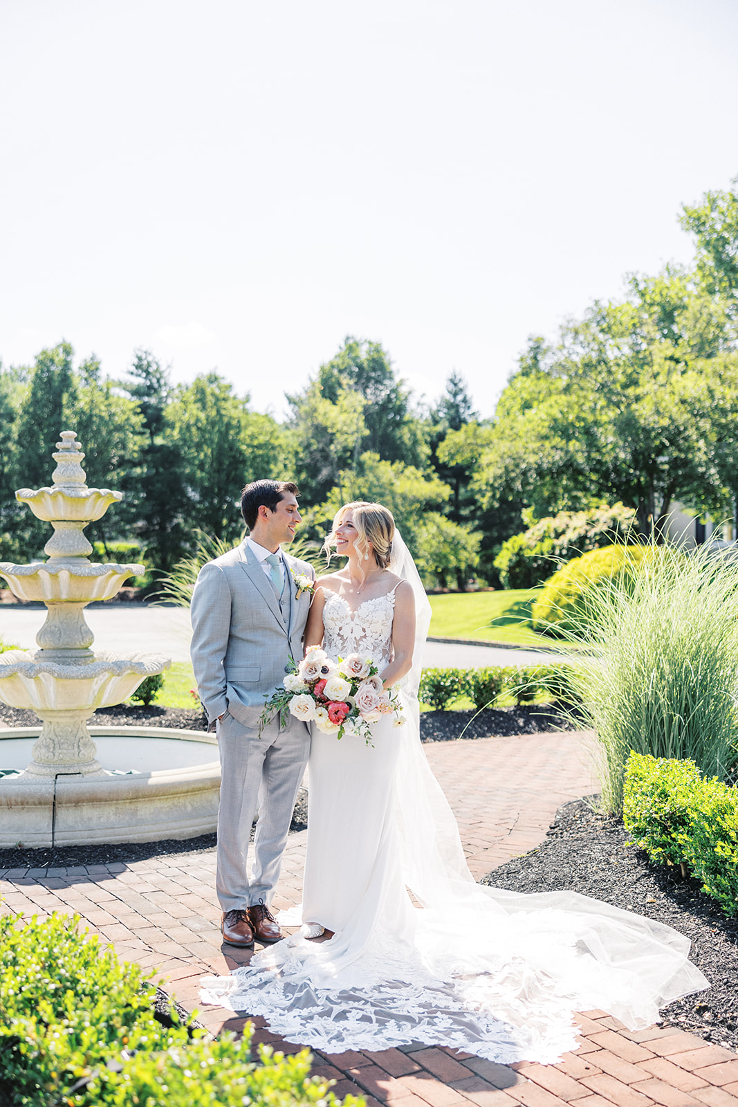 NEwlyweds smile at each other while standing in a garden by a fountain in front of the Pen Ryn Estate Wedding venue