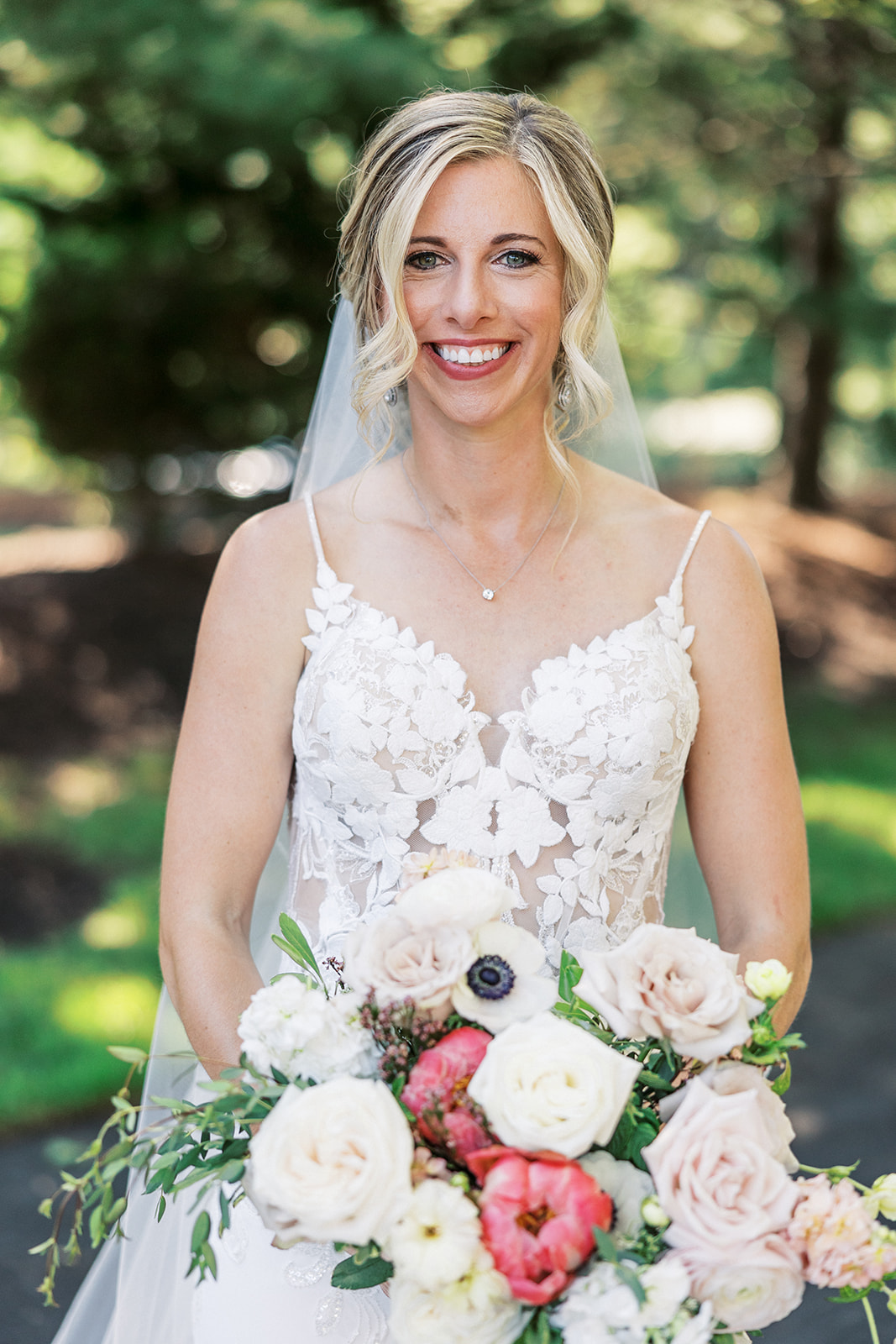 A bride smiles while holding her colorful bouquet in a garden