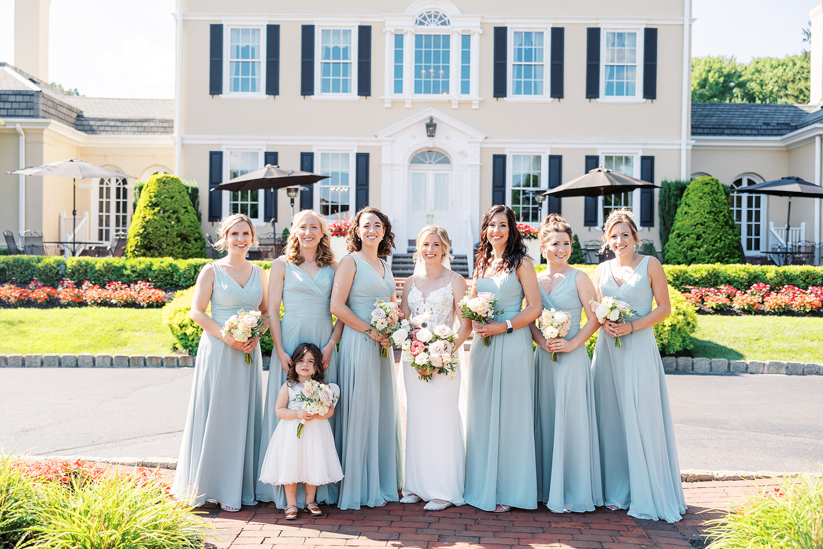 A bride stands with her bridesmaids and flower girl in blue dresses outside the front entrance of their venue