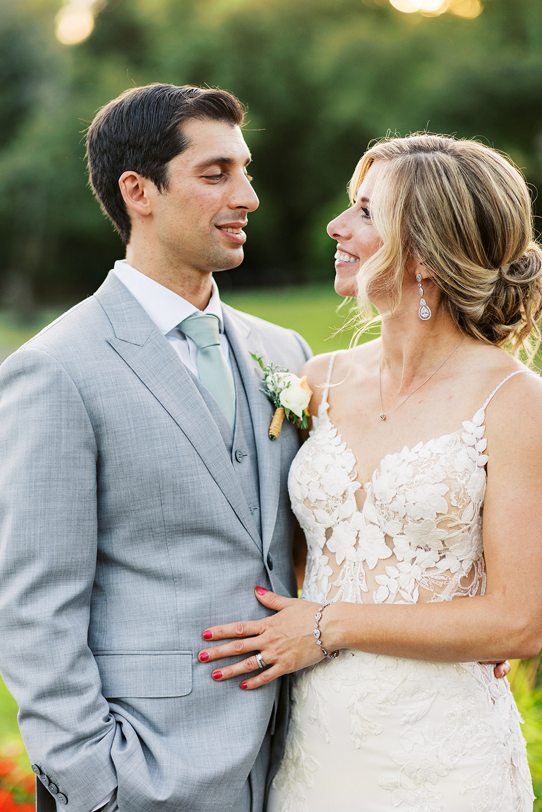 Newlyweds smile at each other while standing in a garden at sunset