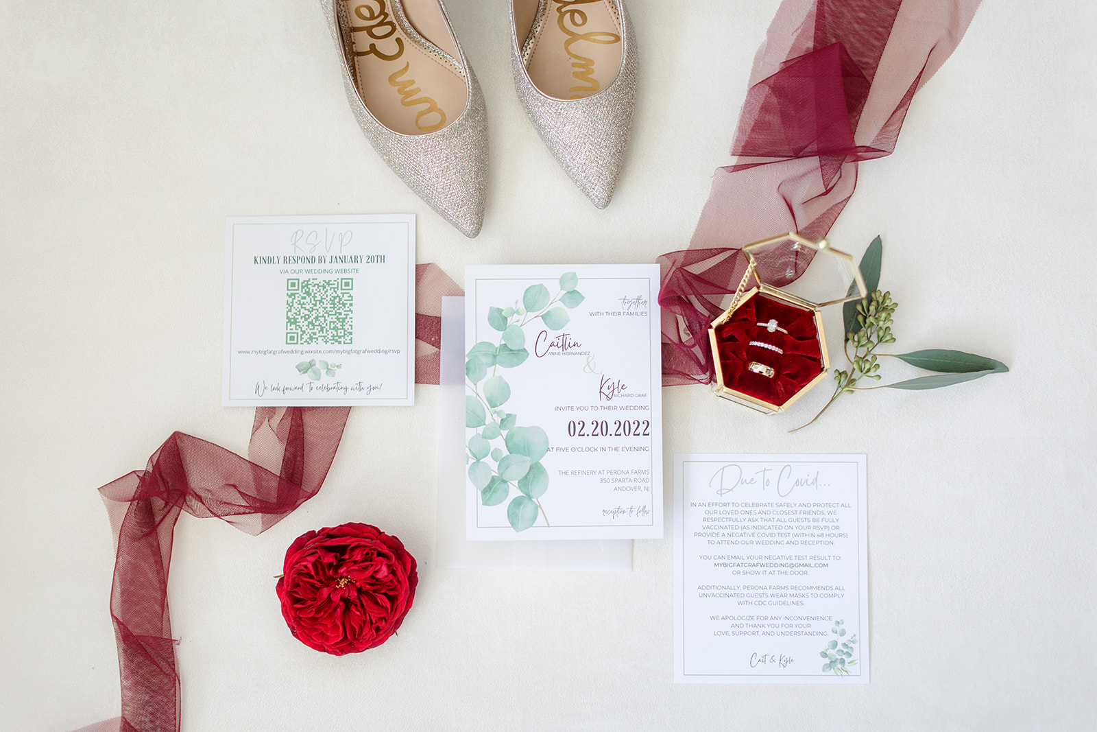 bridal details of rings, roses and invitations sit on a white table