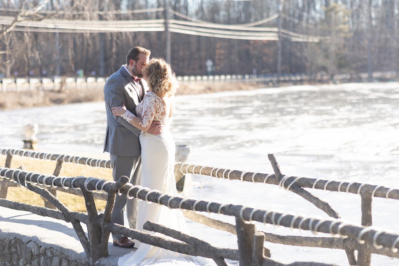 Newlyweds kiss while standing on a rustic bridge over a river at their The Refinery At Perona Farms wedding