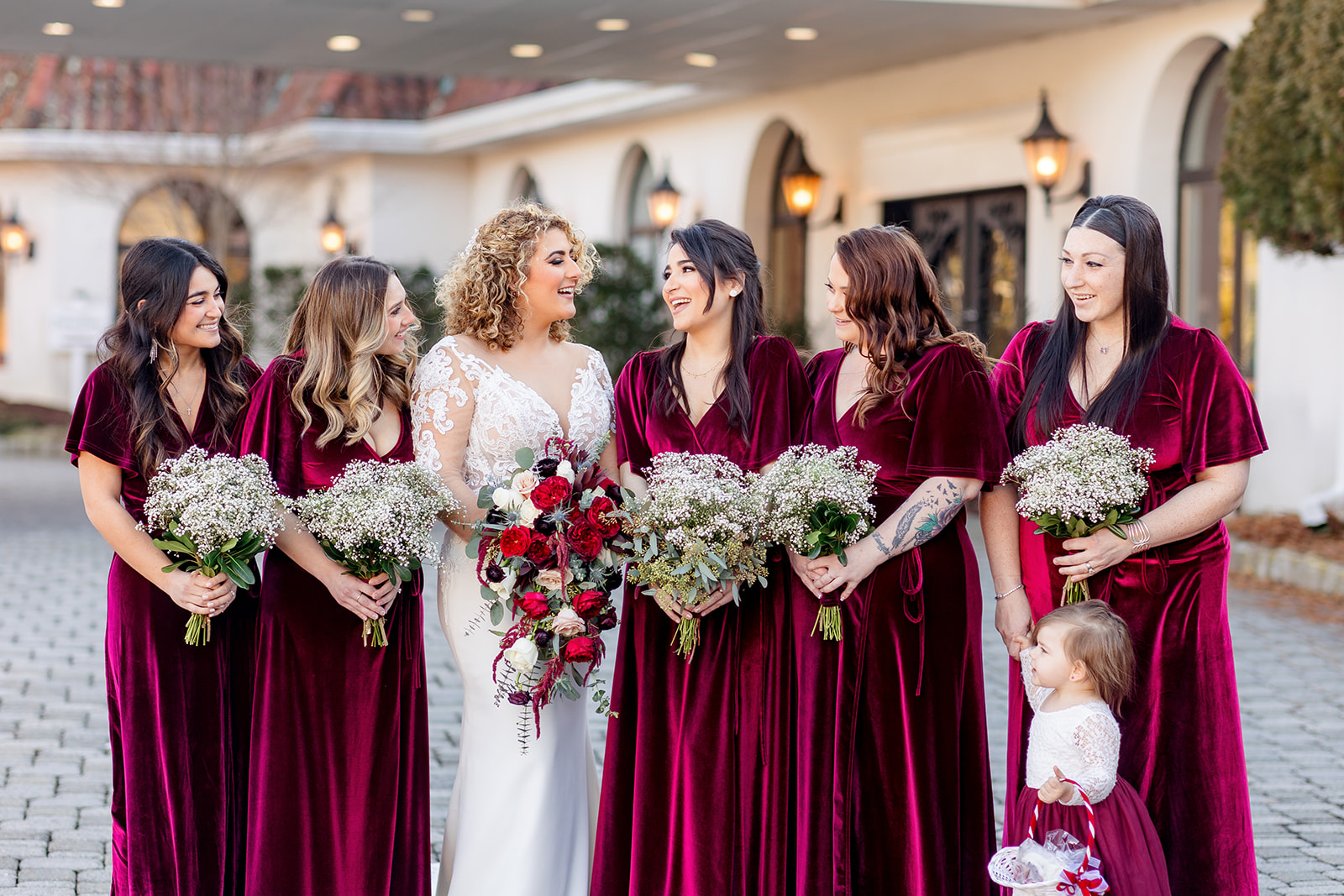 A bride stands with her bridesmaids all holding their bouquets in red velvet dresses