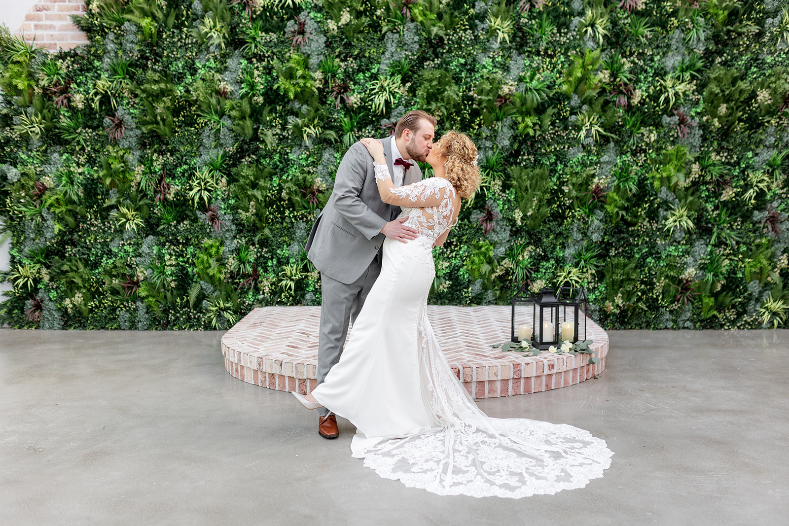 Newlyweds kiss while standing at their greenery wall covered ceremony location at The Refinery At Perona Farms