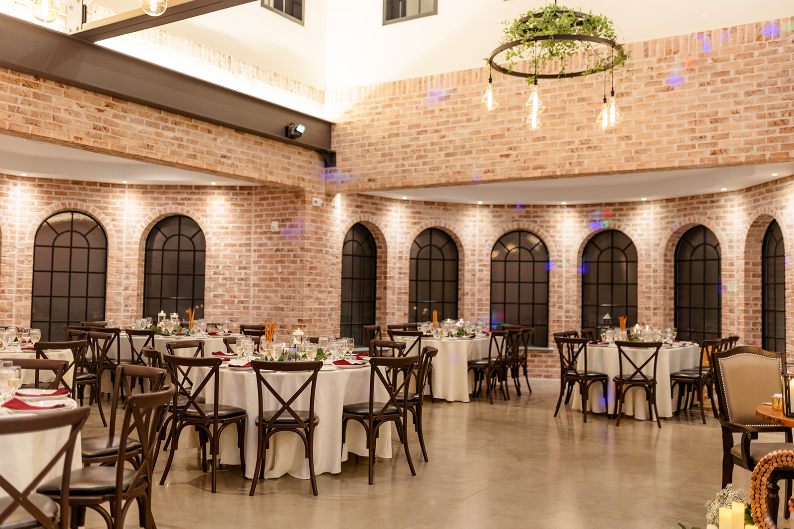 Details of a wedding reception set up in a brick building with white linens and dark chairs