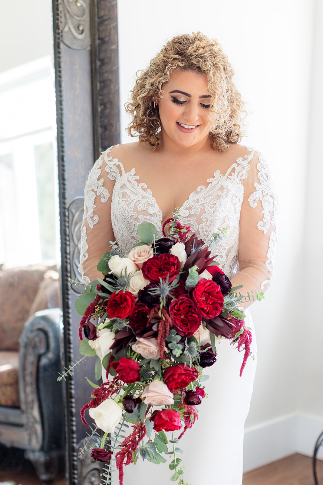 A bride smiles down to her large red bouquet in her hands while standing in the getting ready room