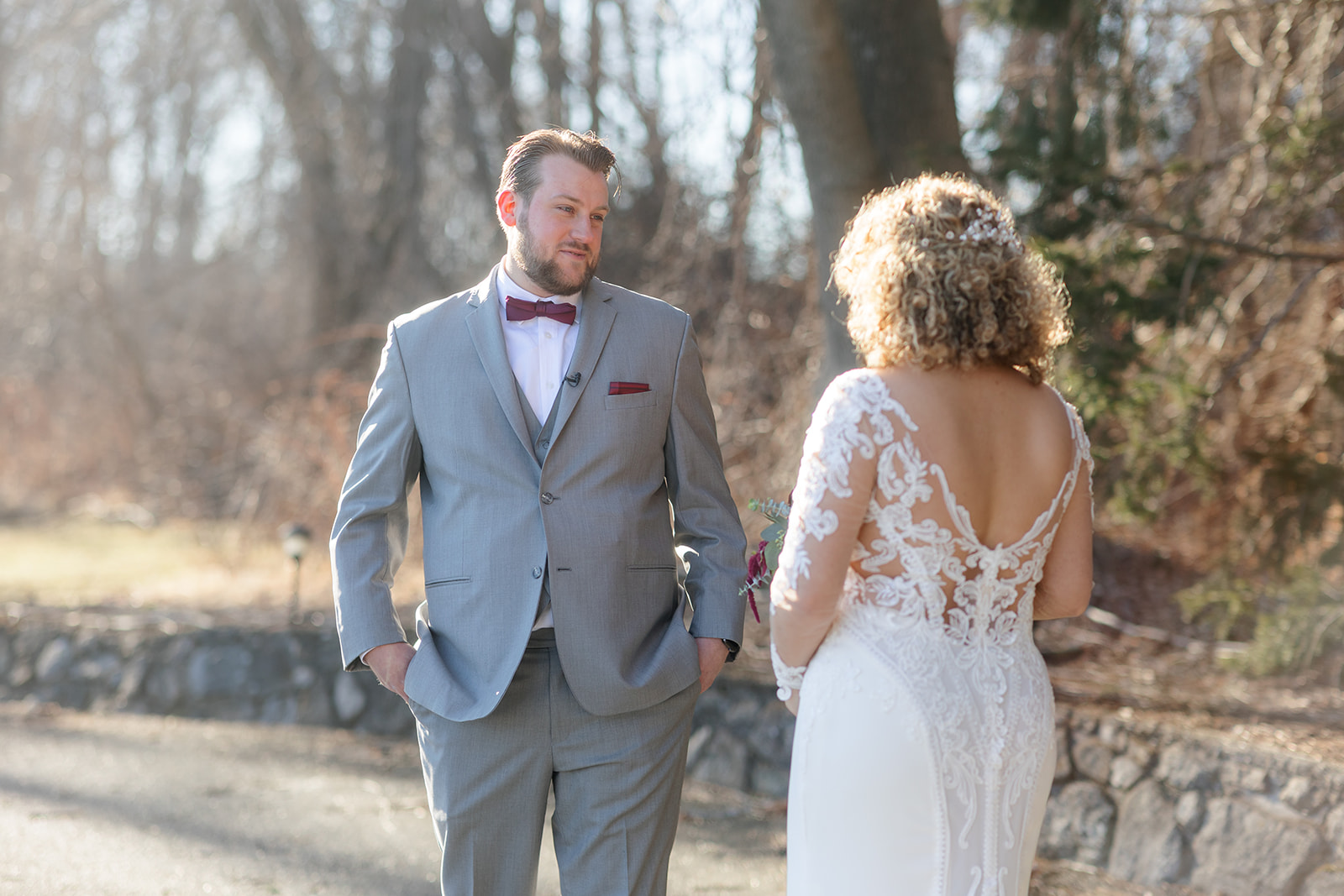A groom in a grey suit sees his bride in her lace dress for the first time during a first look at The Refinery At Perona Farms