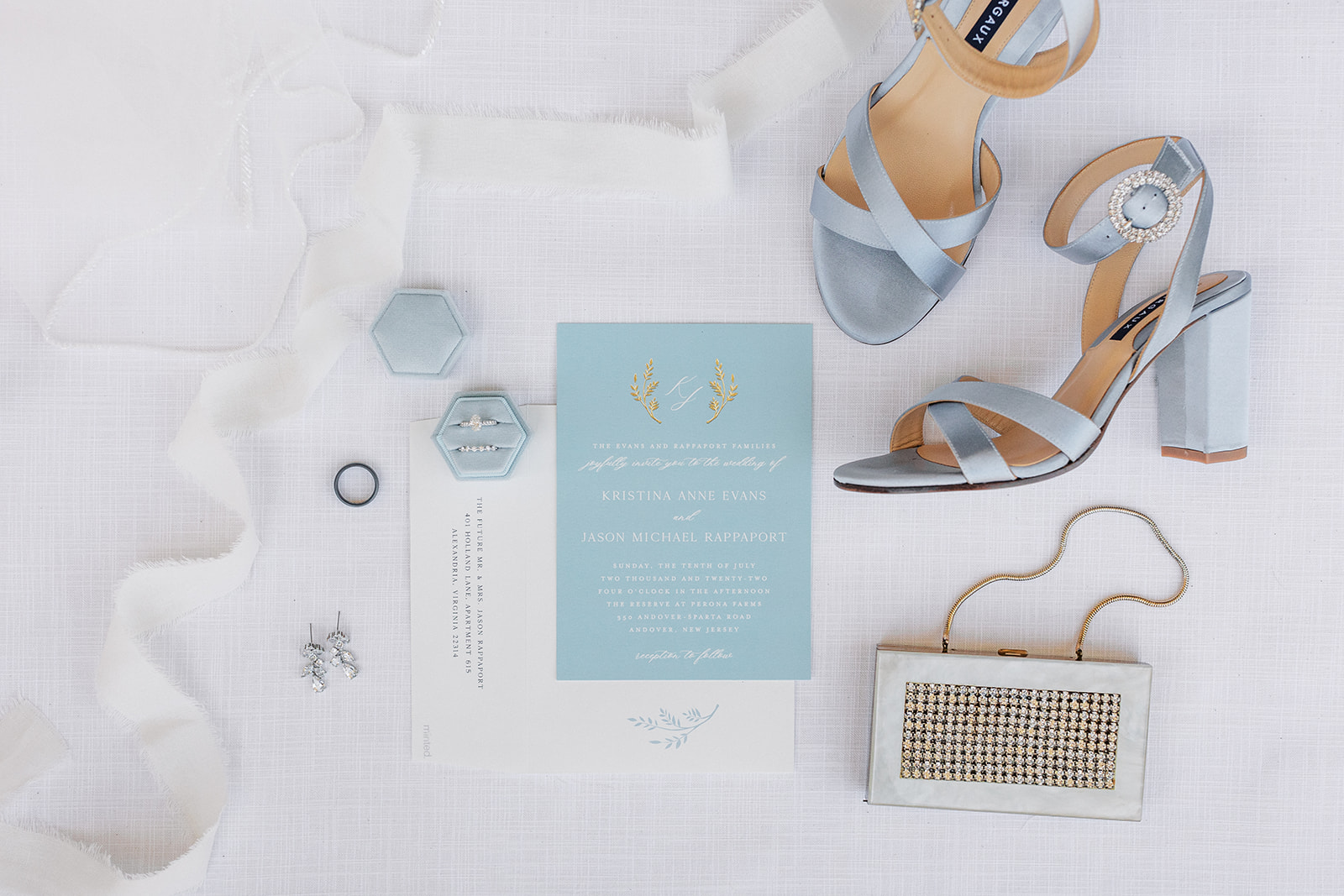 Bridal details of a purse, shoes, rings and earrings sit on a table with invitations