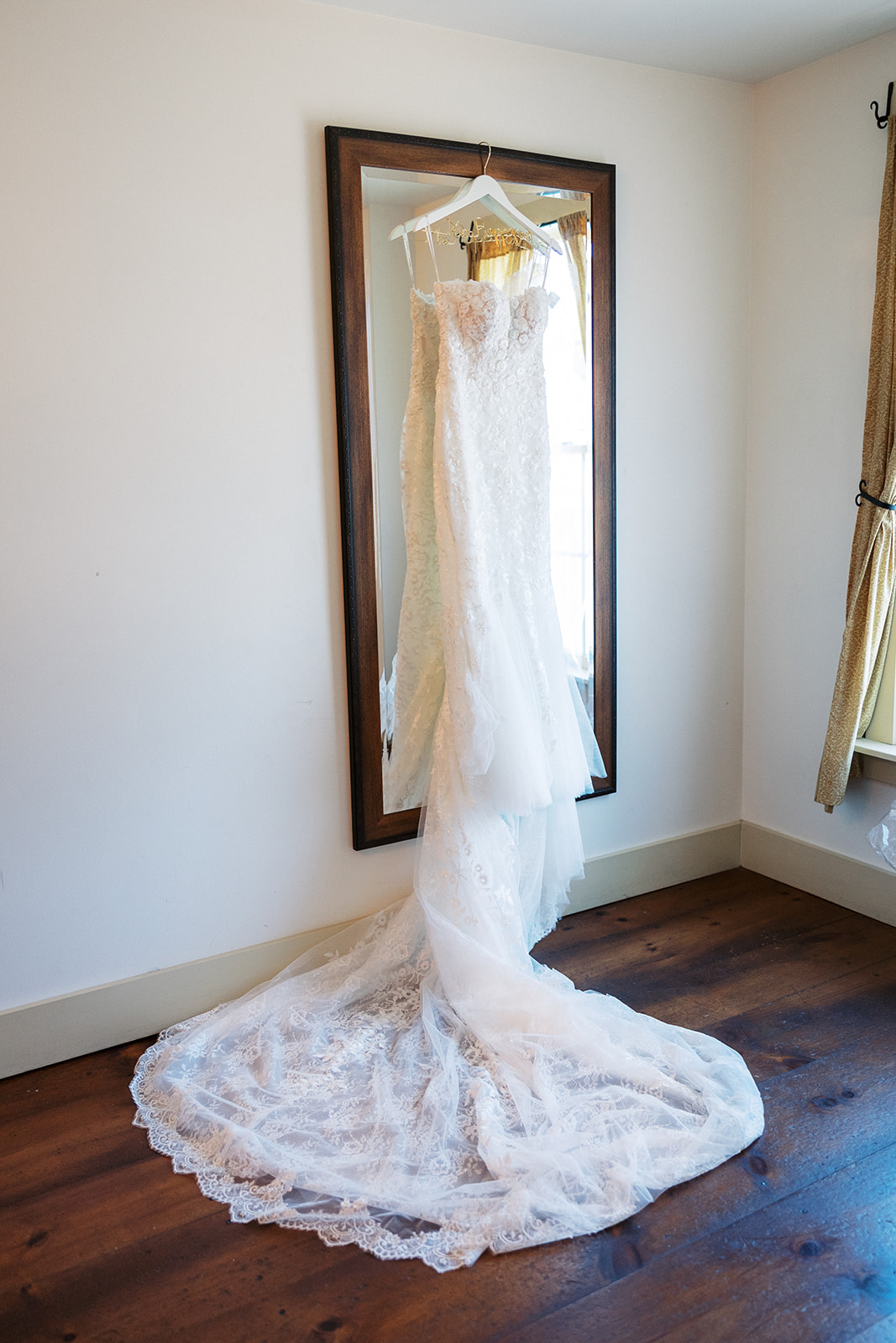 A white lace dress hangs from a mirror with a long train