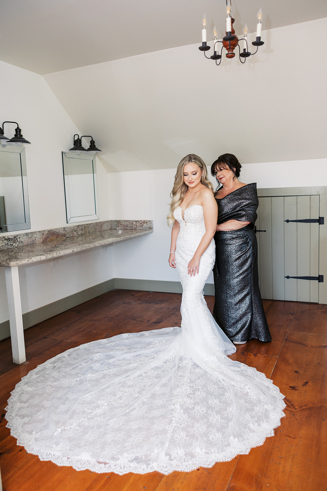A bride is closed into her dress by mom while standing in the getting ready room