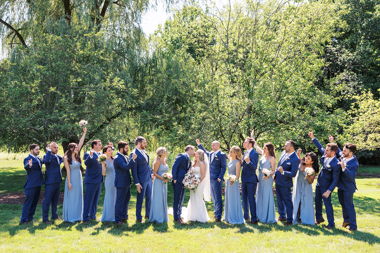 Newlyweds kiss in a lawn while surrounded by their cheering wedding party at their The Reserve At Perona Farms wedding