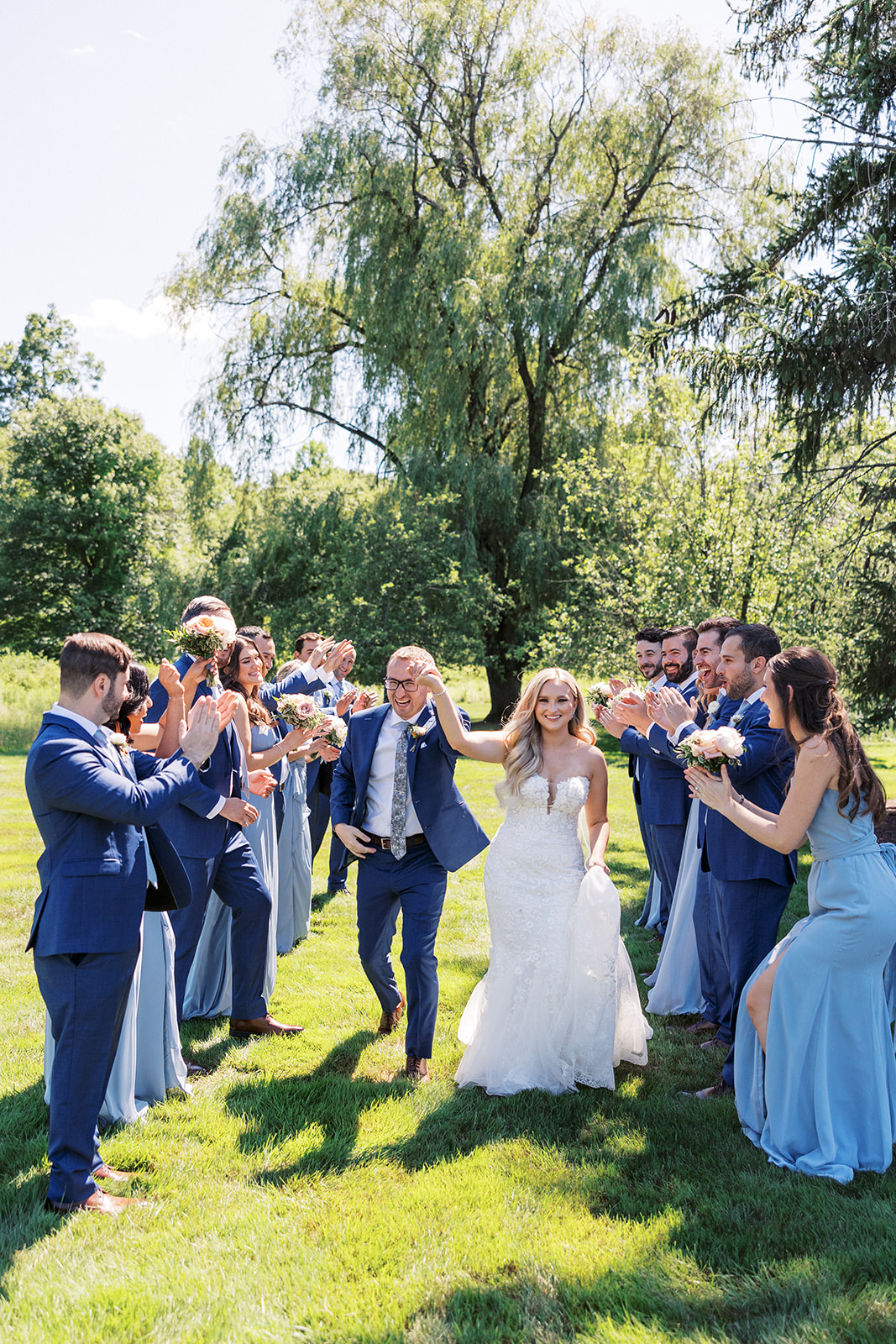 Newlyweds hold hands while walking through a path in a lawn made by their applauding wedding party