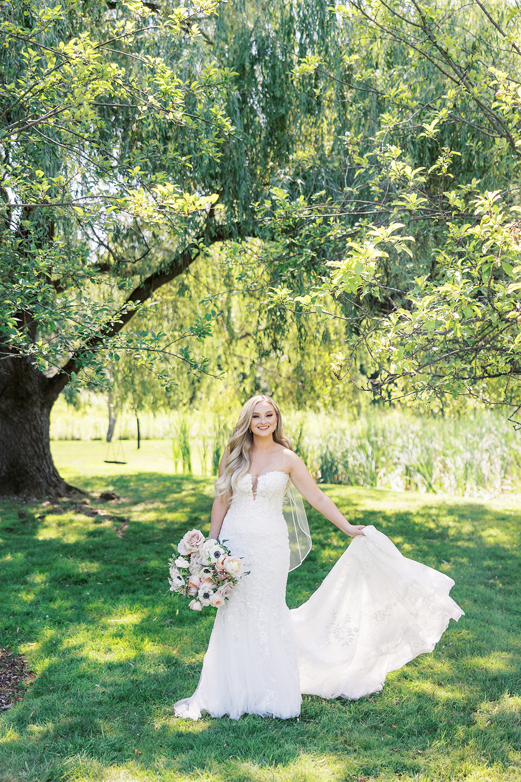 A bride walks through a grassy lawn under a willow tree at her The Reserve At Perona Farms wedding
