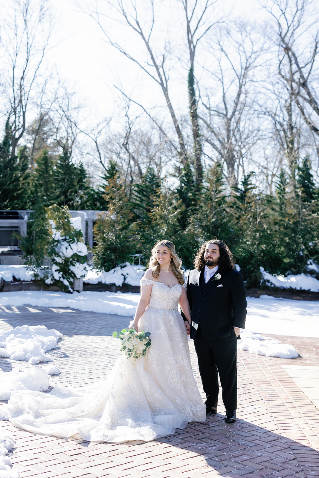 Newlyweds walk up a brick patio covered in snow at their Crest Hollow Country Club Wedding