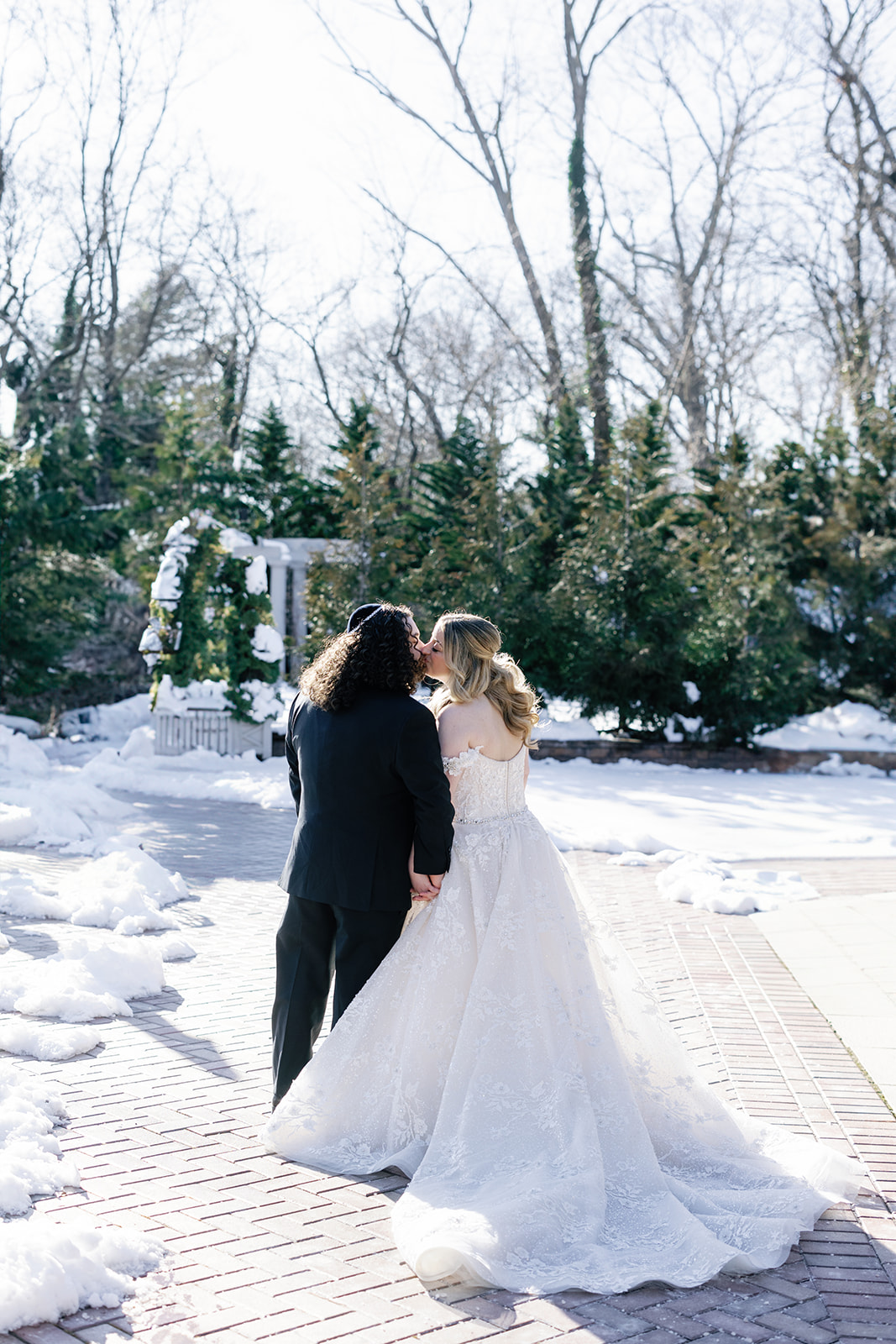 Newlyweds share a kiss while holding hands and standing on a snow covered patio at their Crest Hollow Country Club Wedding