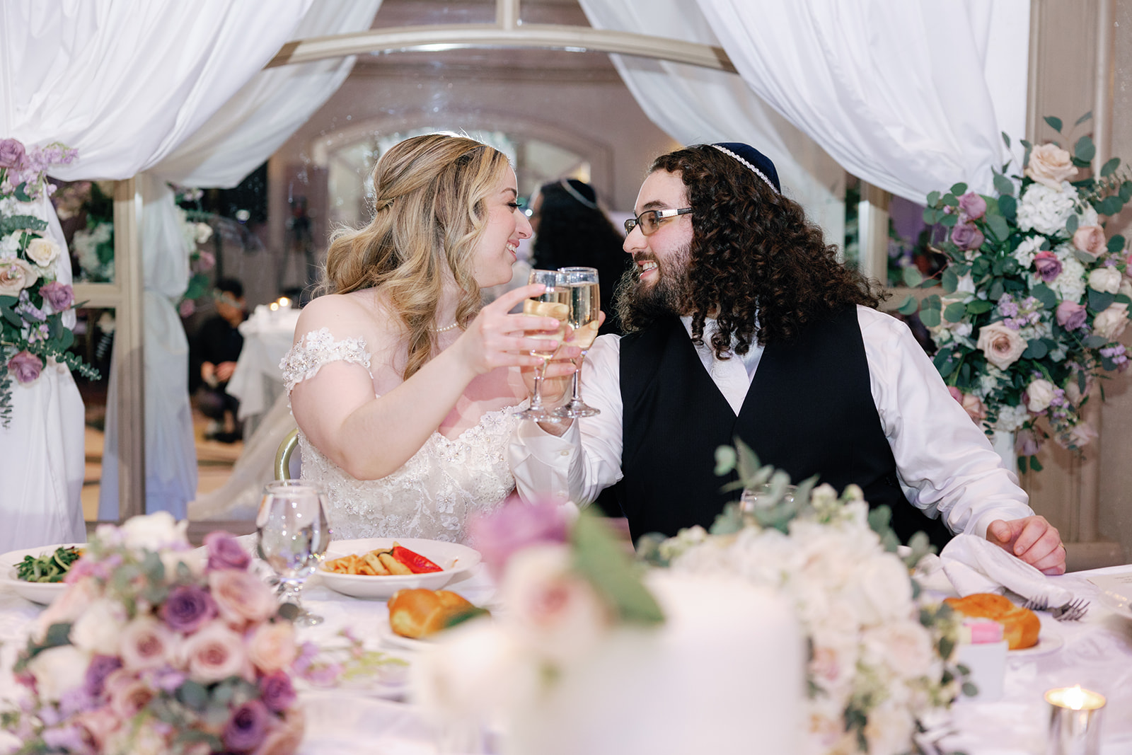 Newlyweds share a toast of champagne while sitting at their head table in front of a mirror