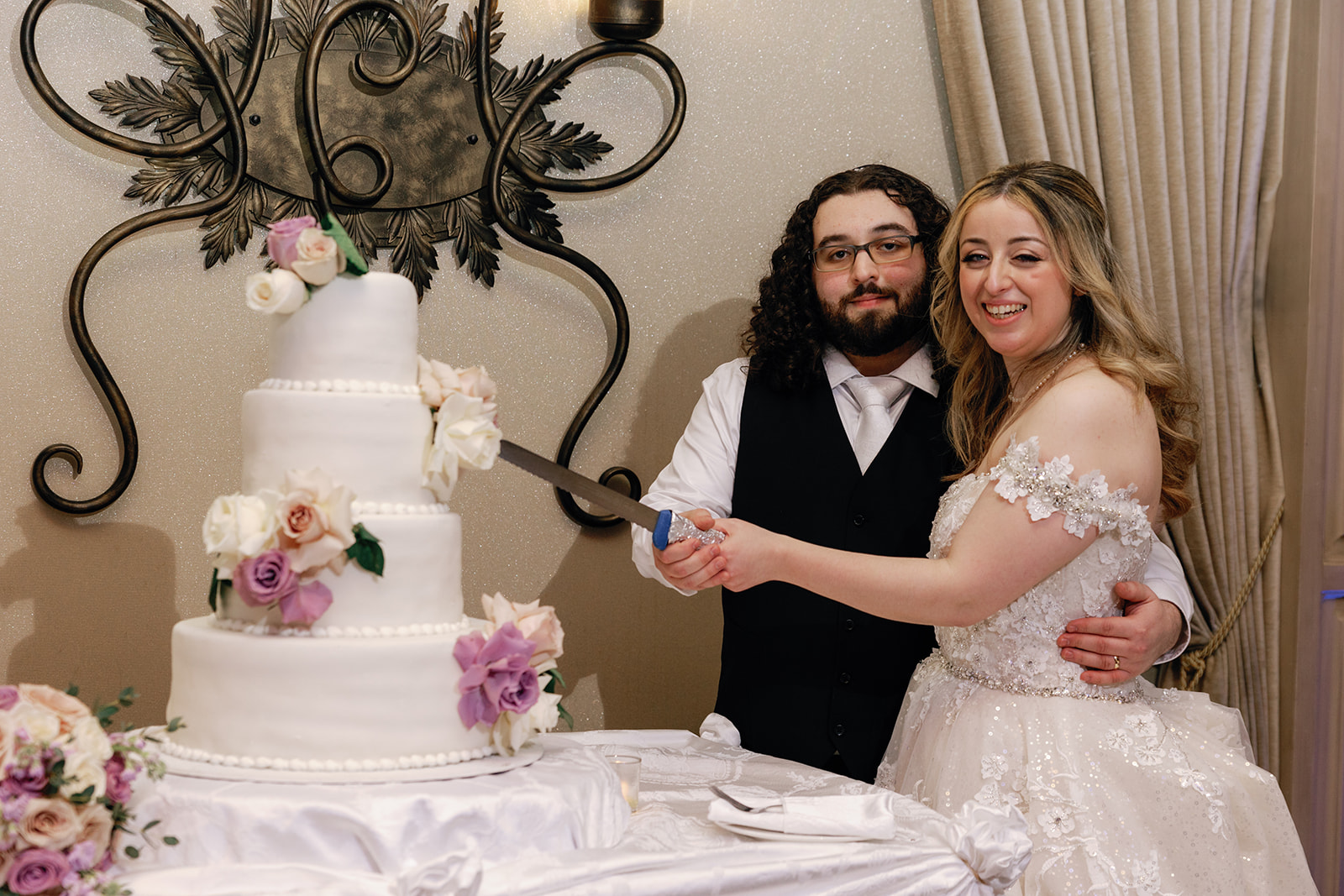 Newlyweds laugh and smile while preparing to cut their four tier cake at their Crest Hollow Country Club Wedding