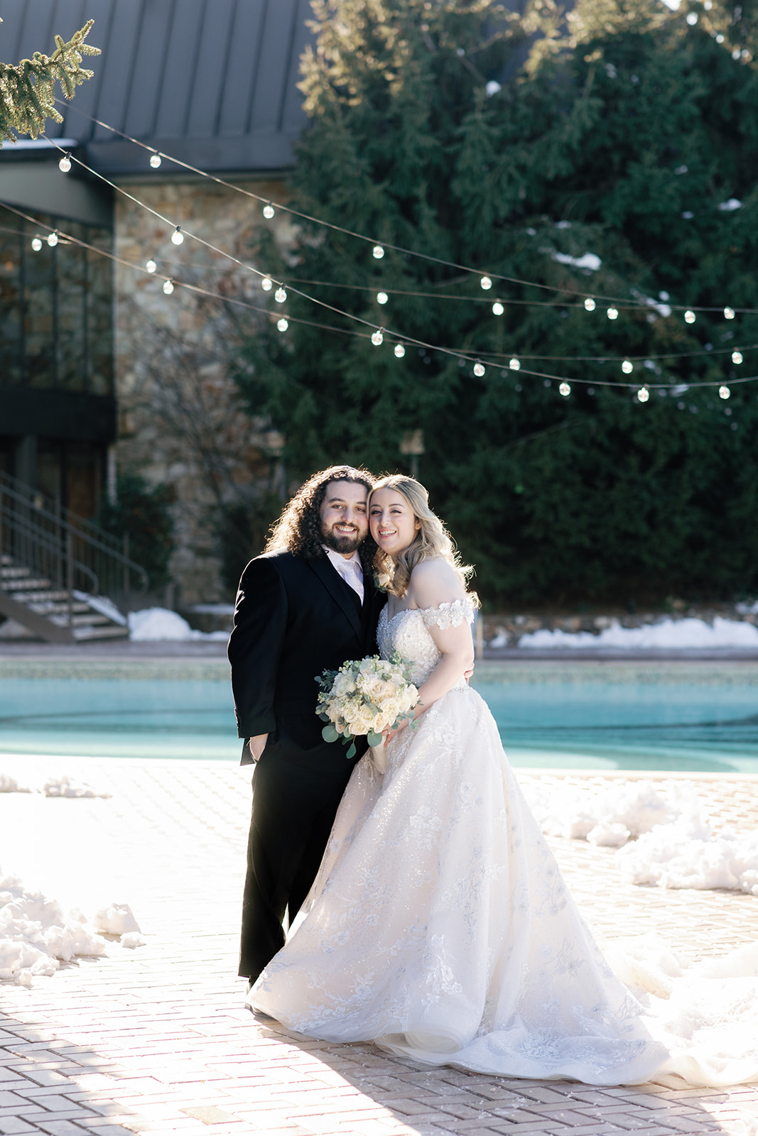 Newlyweds touch cheeks while standing on a snow covered pool patio at their Crest Hollow Country Club Wedding
