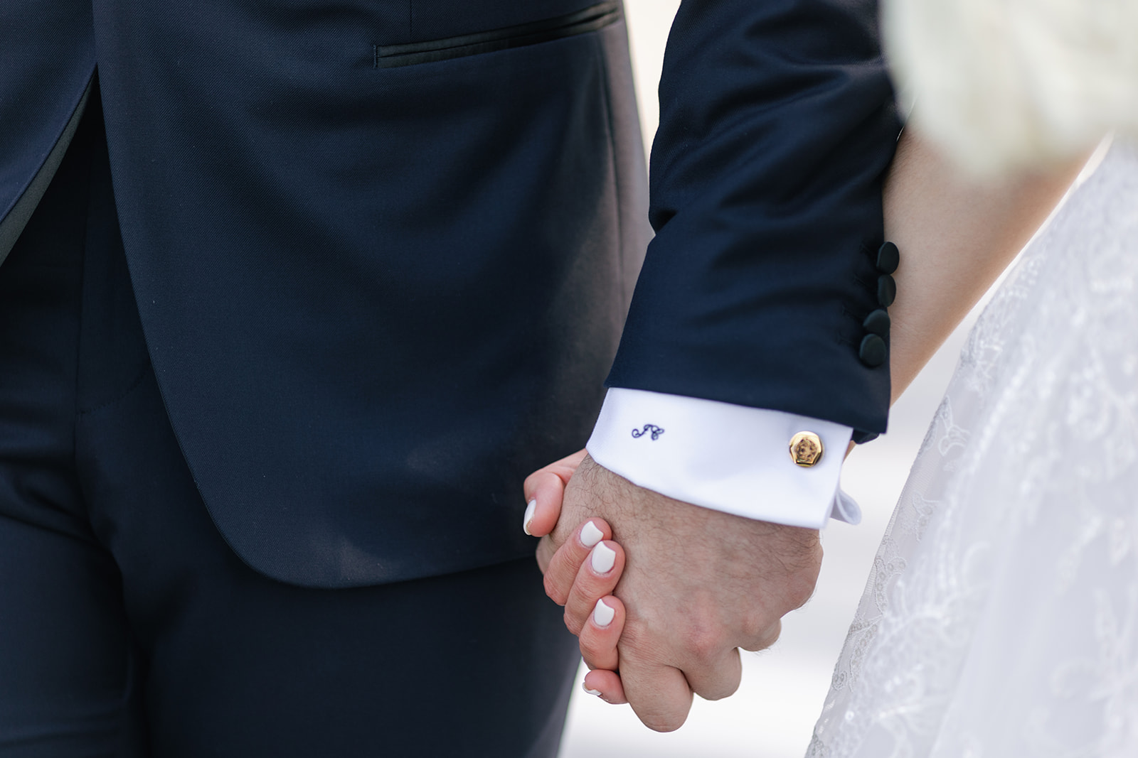 Details of newlyweds holding hands with custom cufflinks and embroidery on the suit