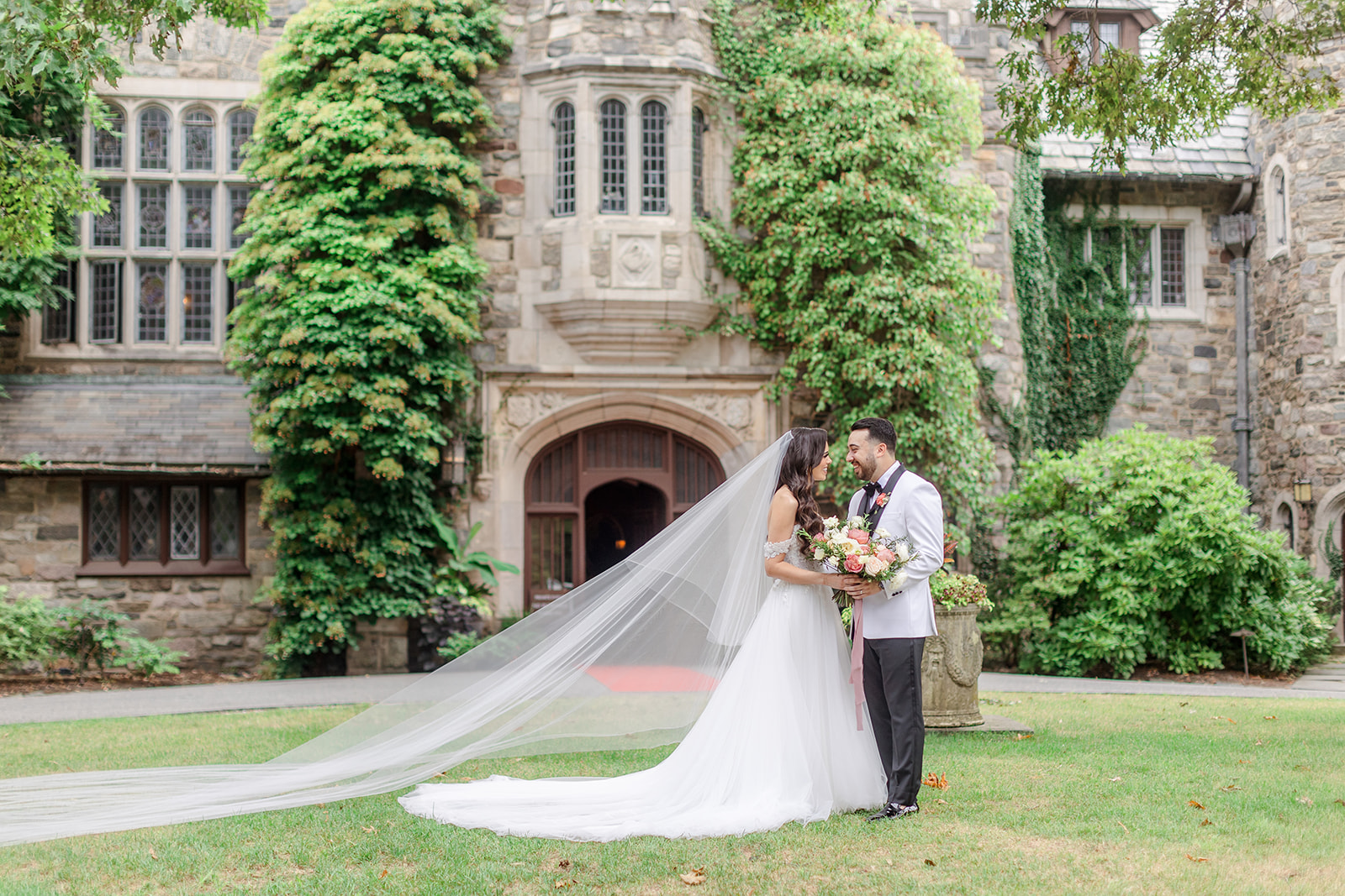 Newlyweds laugh while holding the colorful bouquet outside a castle