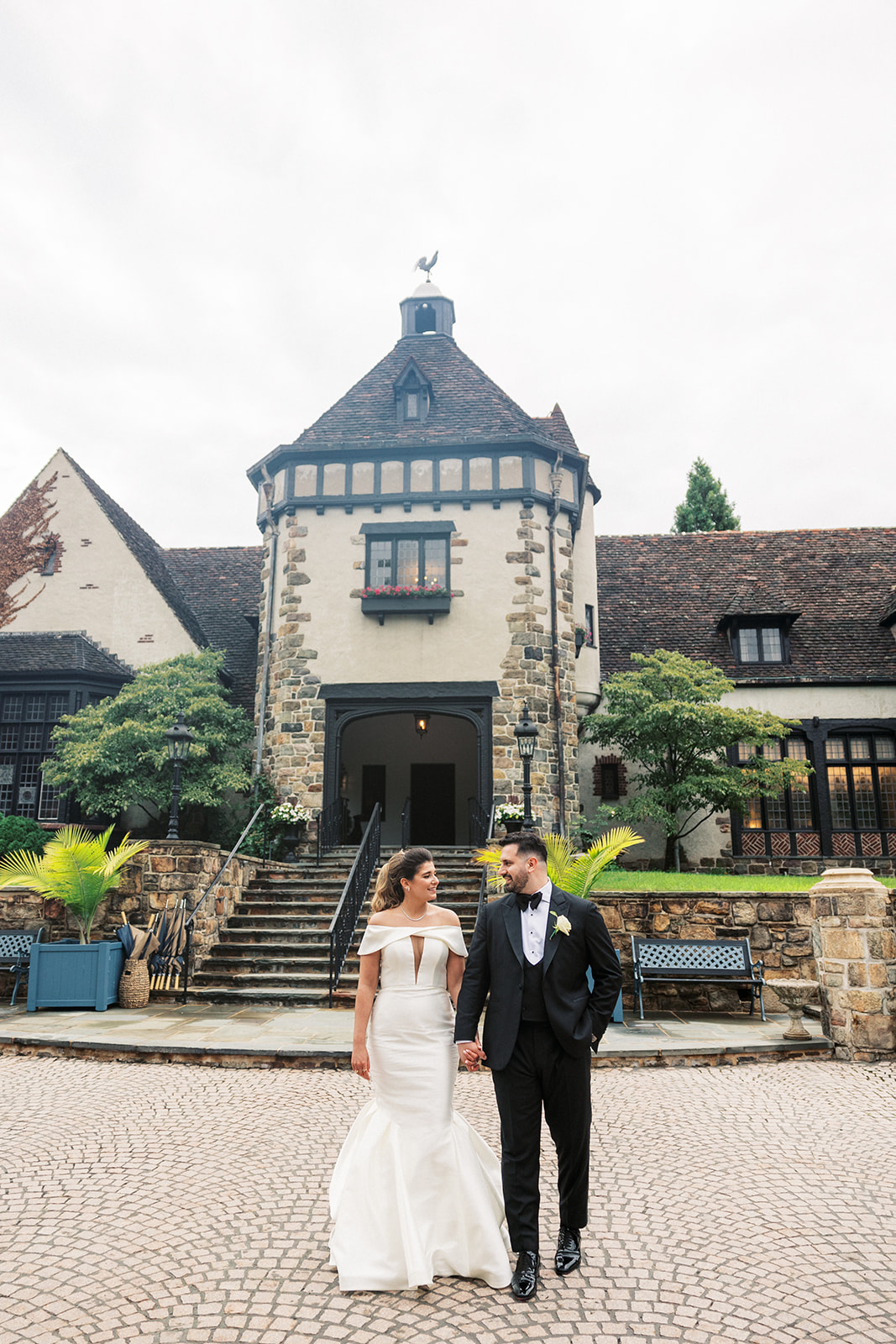 Newlyweds smile at each other while holding hands and walking outside their venue