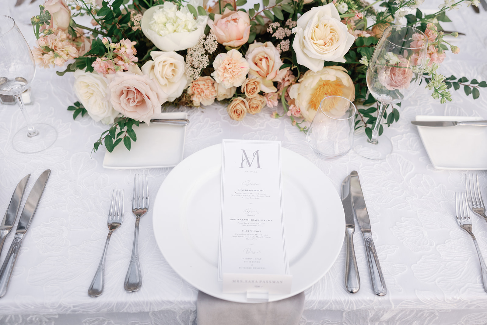 Details of a wedding reception table setting on white embroidered linen with silver silverware